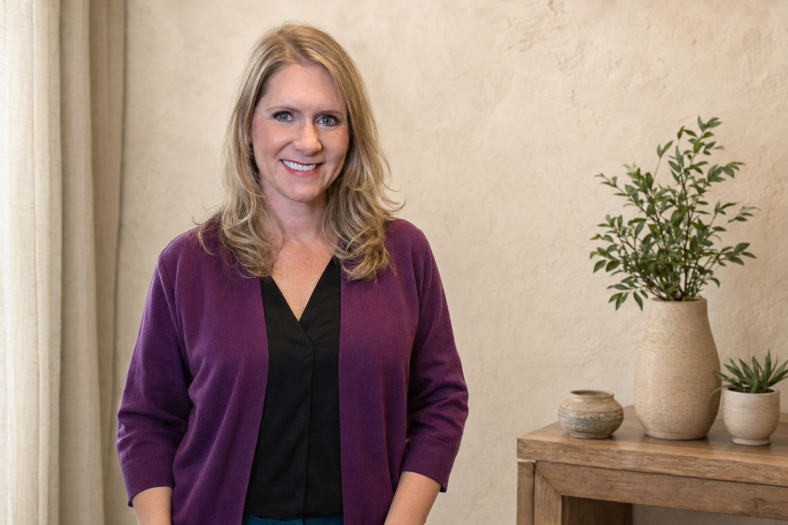 Dr. Diane Otness standing in a warm, softly lit room with plants on a wooden console table